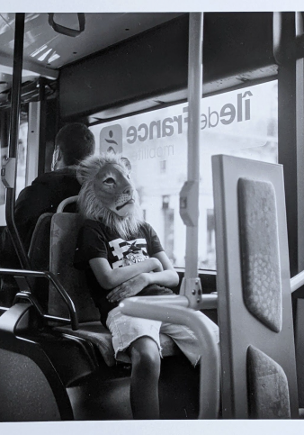 Photographie en noir et blanc d'un enfant avec un masque de lion assis dans un bus